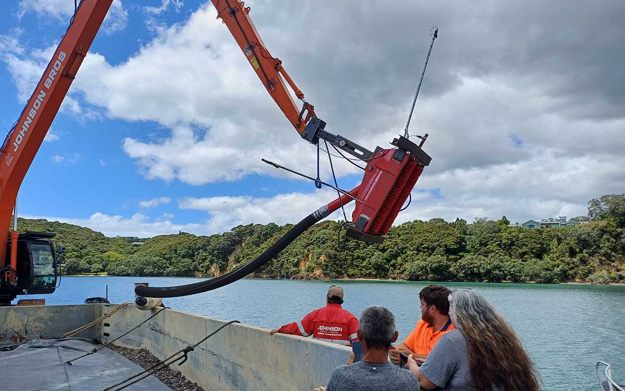 Crane removing Caulerpa with people watching by water.