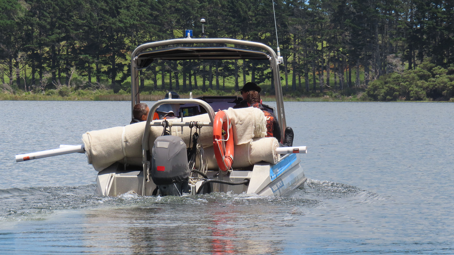 A boat on the water with large rolls of wool mat on the back.