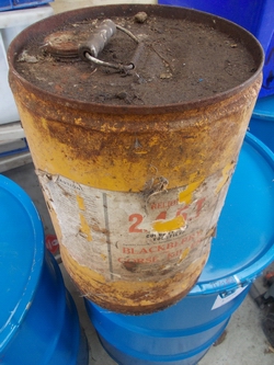 Description: A container of 2,4,5-T herbicide on top of drums of waste. 