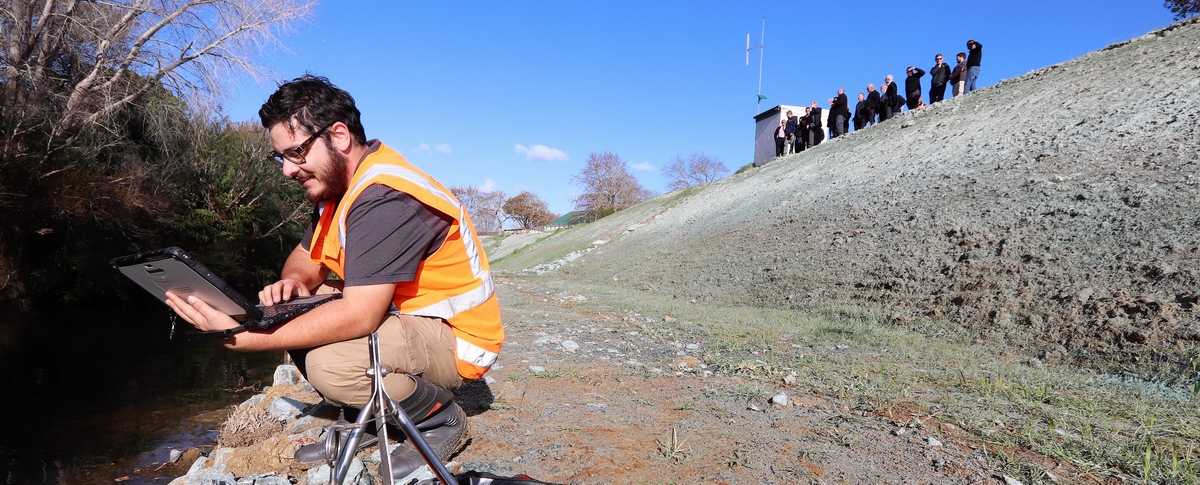 Man holding laptop monitoring river.