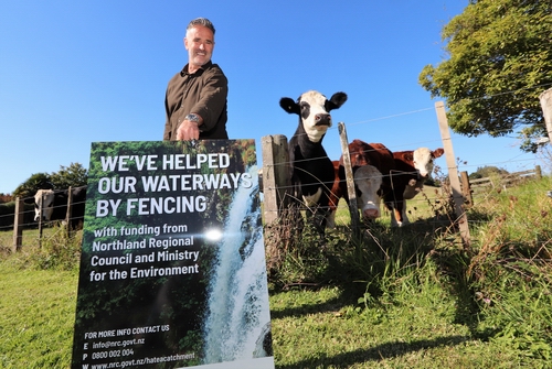 David Sinclair holds a sign by fenced in cows.