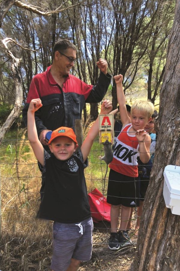 Man and children with rat in trap.