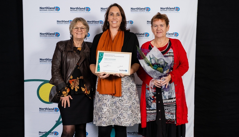 Three women holding certificate and bouquet.