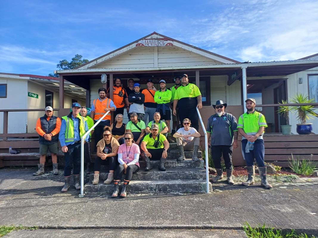 A group of kaimahi wearing hi-viz gathered for a group photo outside a marae.