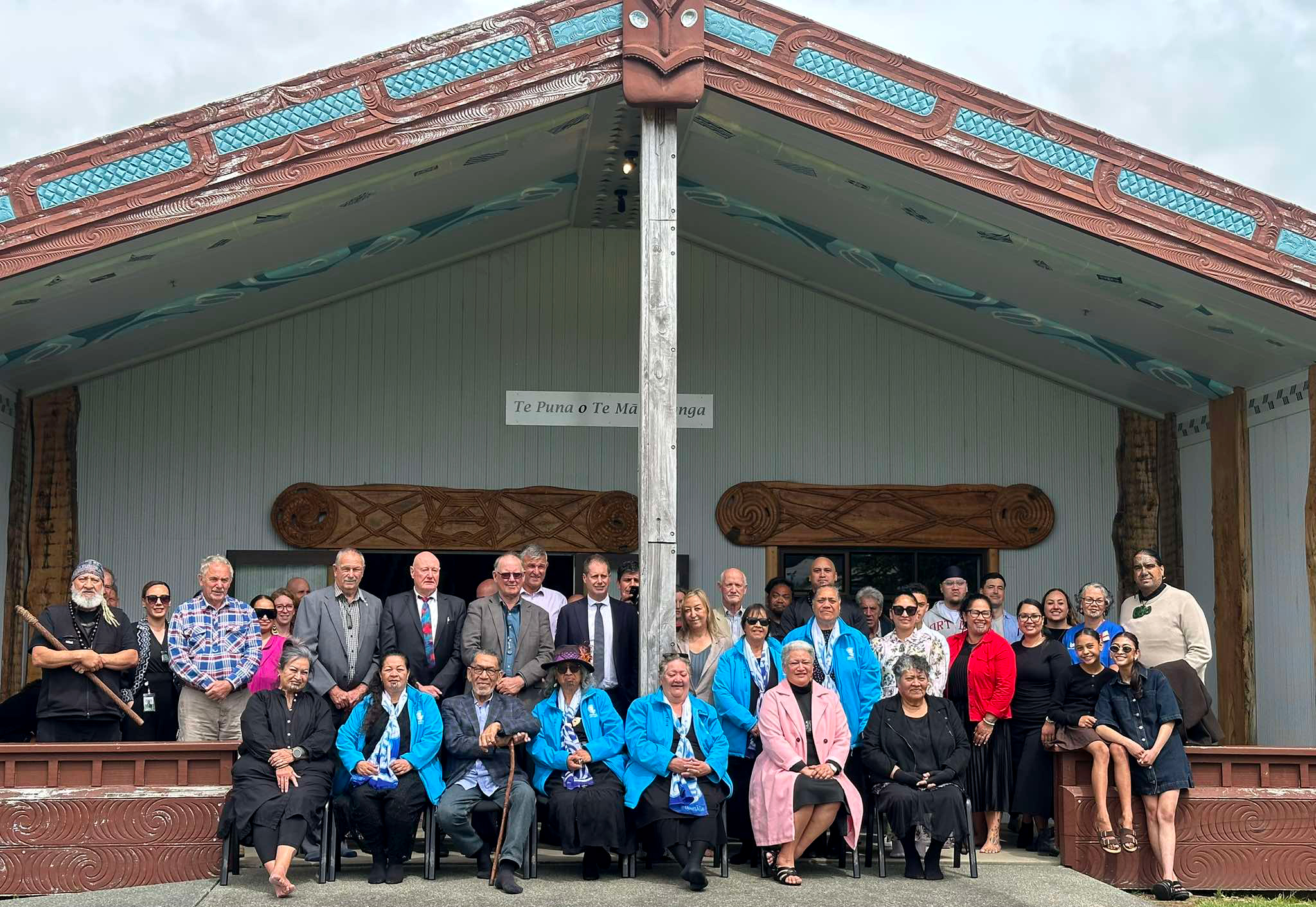 A group of people seated and standing in front of a marae.