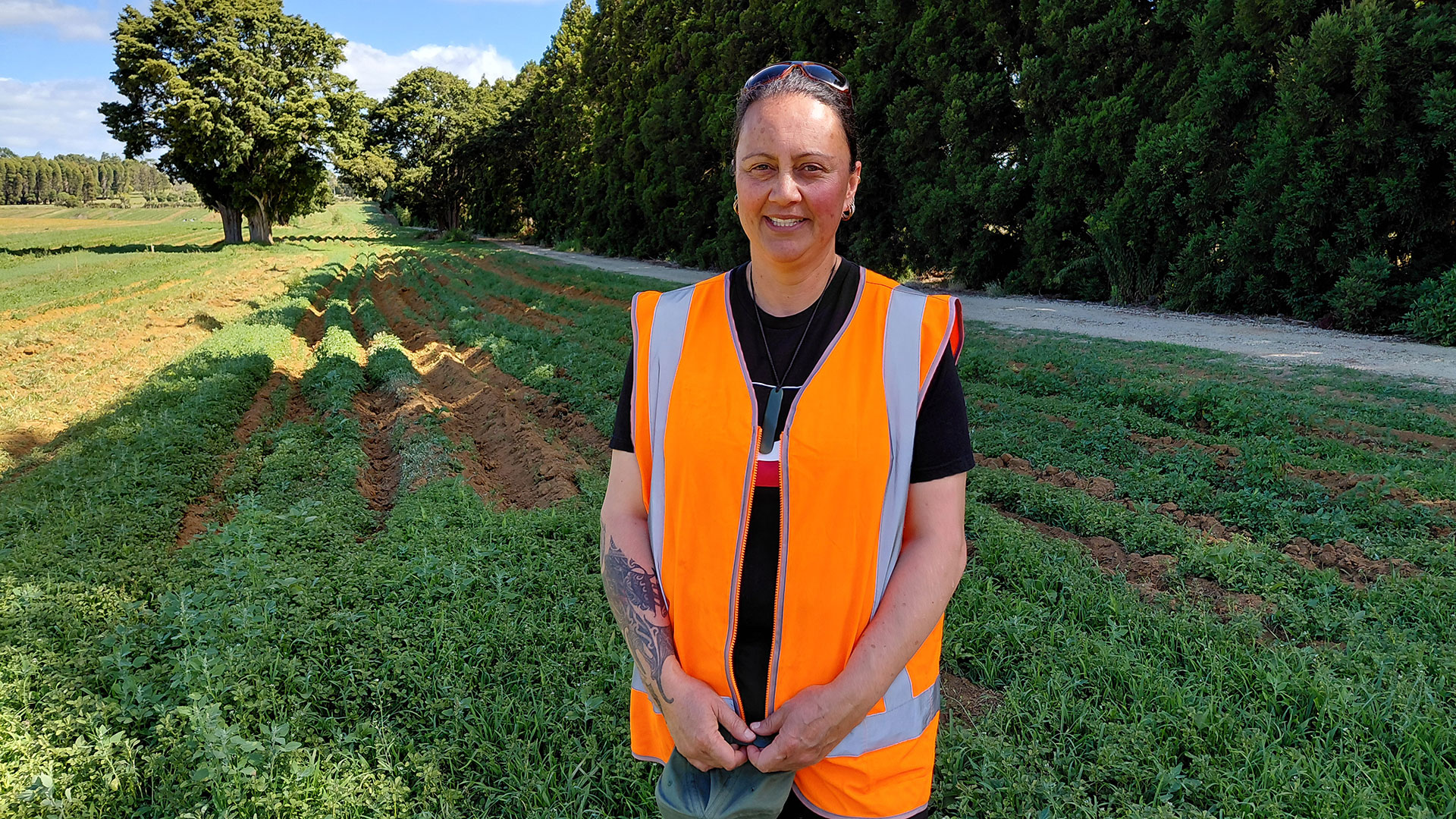 Woman wearing hi-vis vest in a field with trees in the background.
