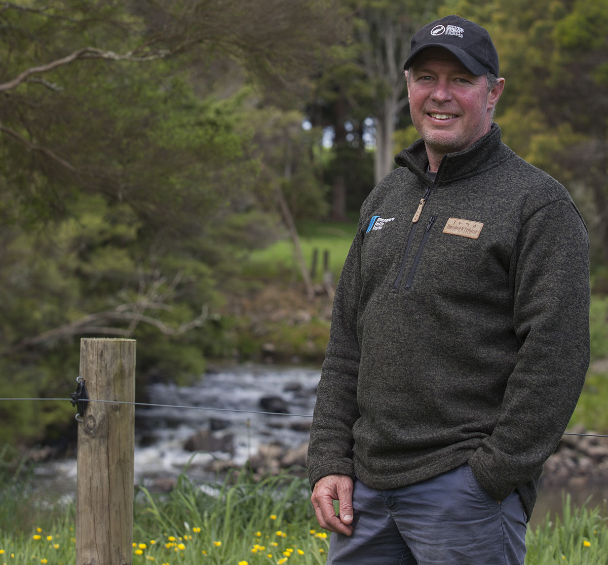 Farmer standing by fenced stream.
