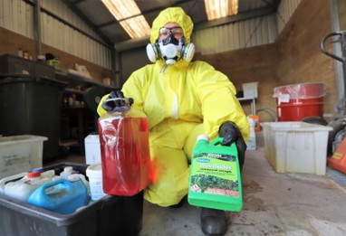 NRC Staff Member in yellow hazardous waste suit with bottle of weed killer and mystery waste (possibly coolant)