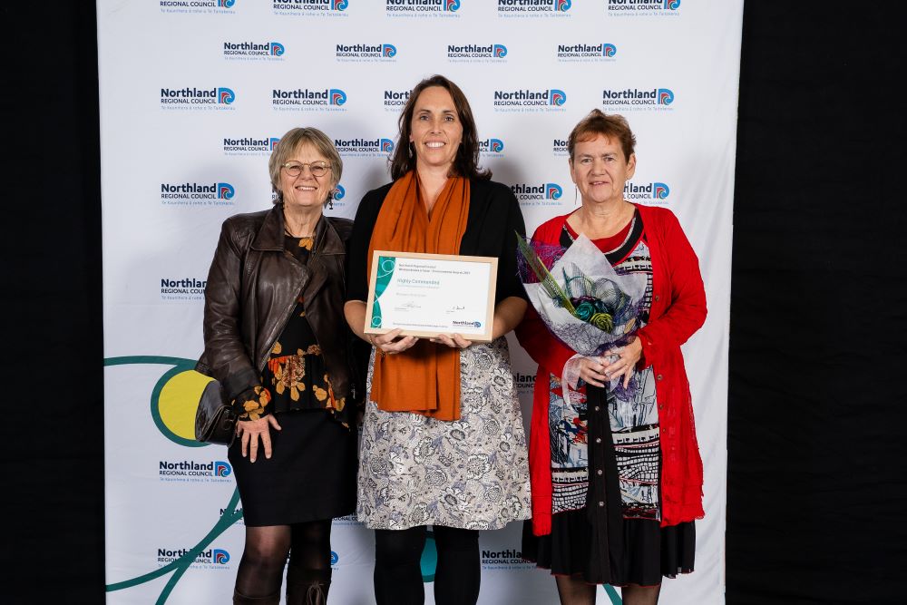 Three women holding certificate and bouquet.