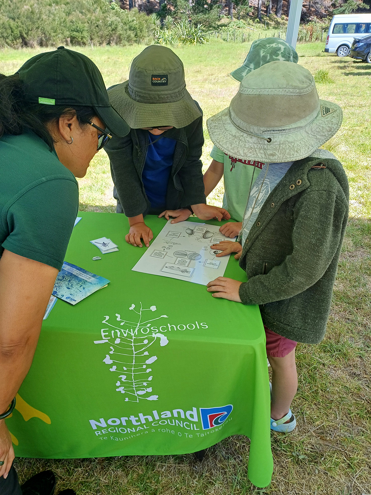 Children lean over paper and read at a table.