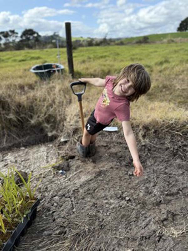 Young child standing with a spade in soil.