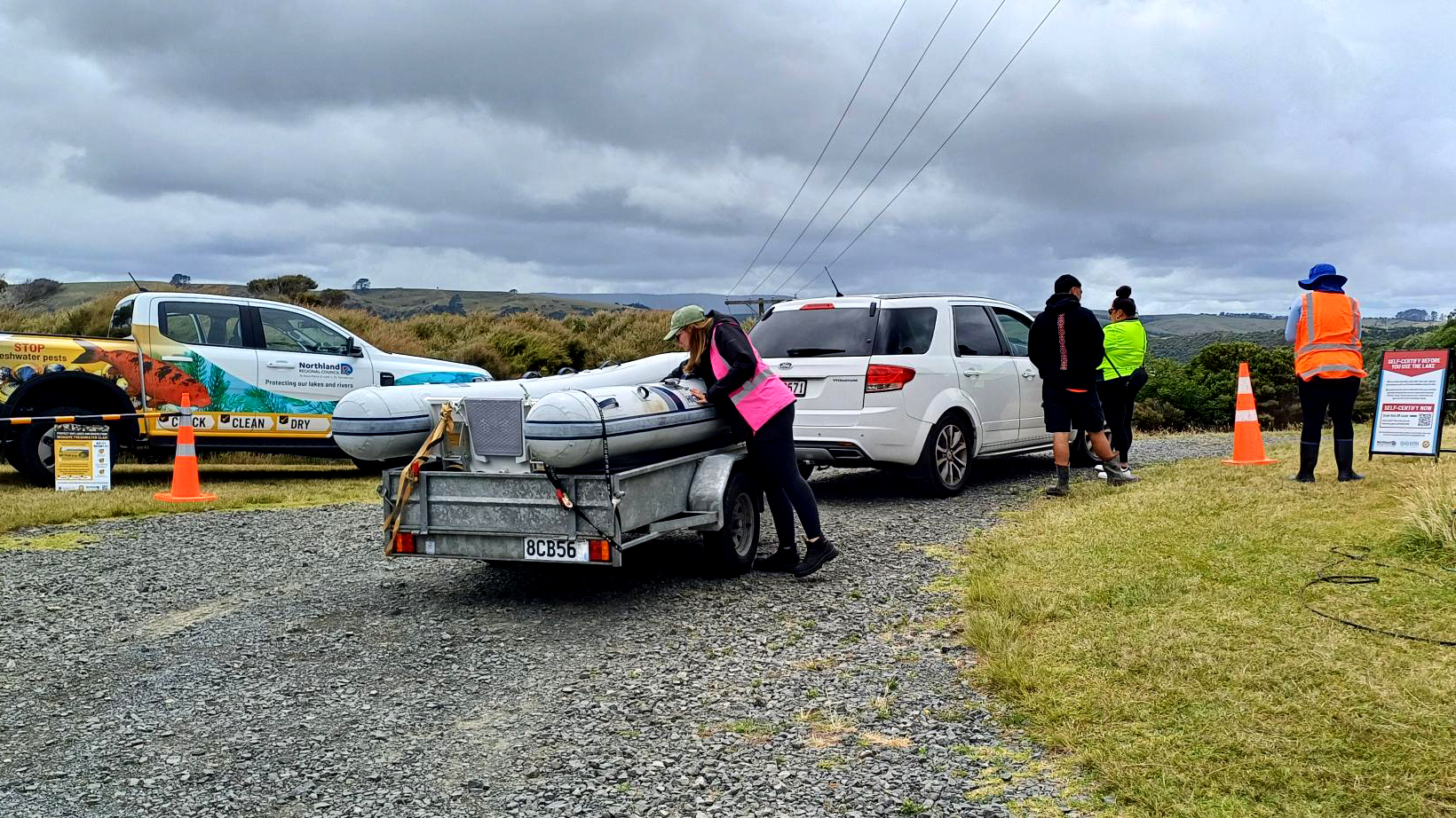 white car with trailer and inflatable boat being inspected by woman wearing pink hi vis vest.