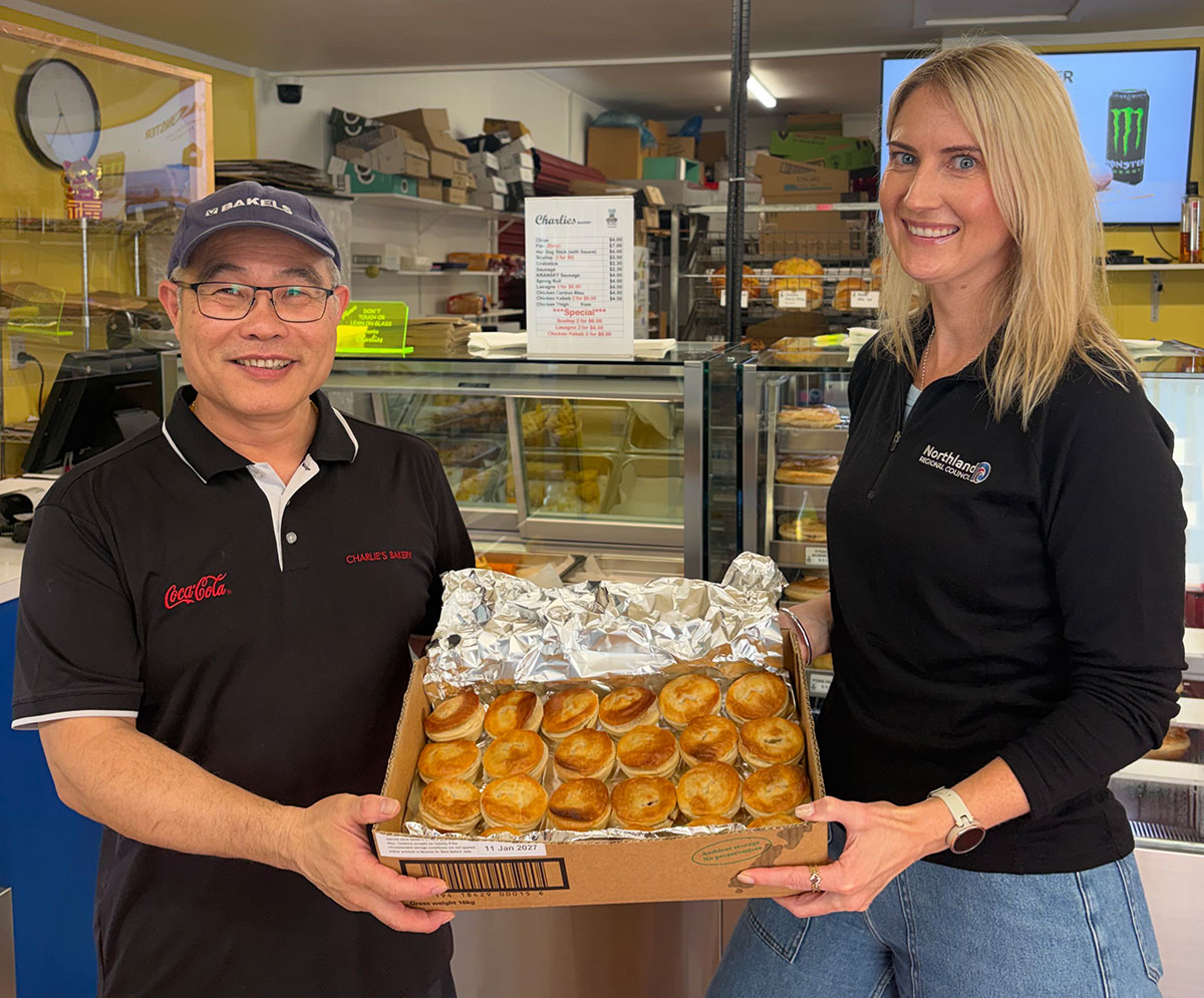Man and woman each hold the side of a box of small pies.