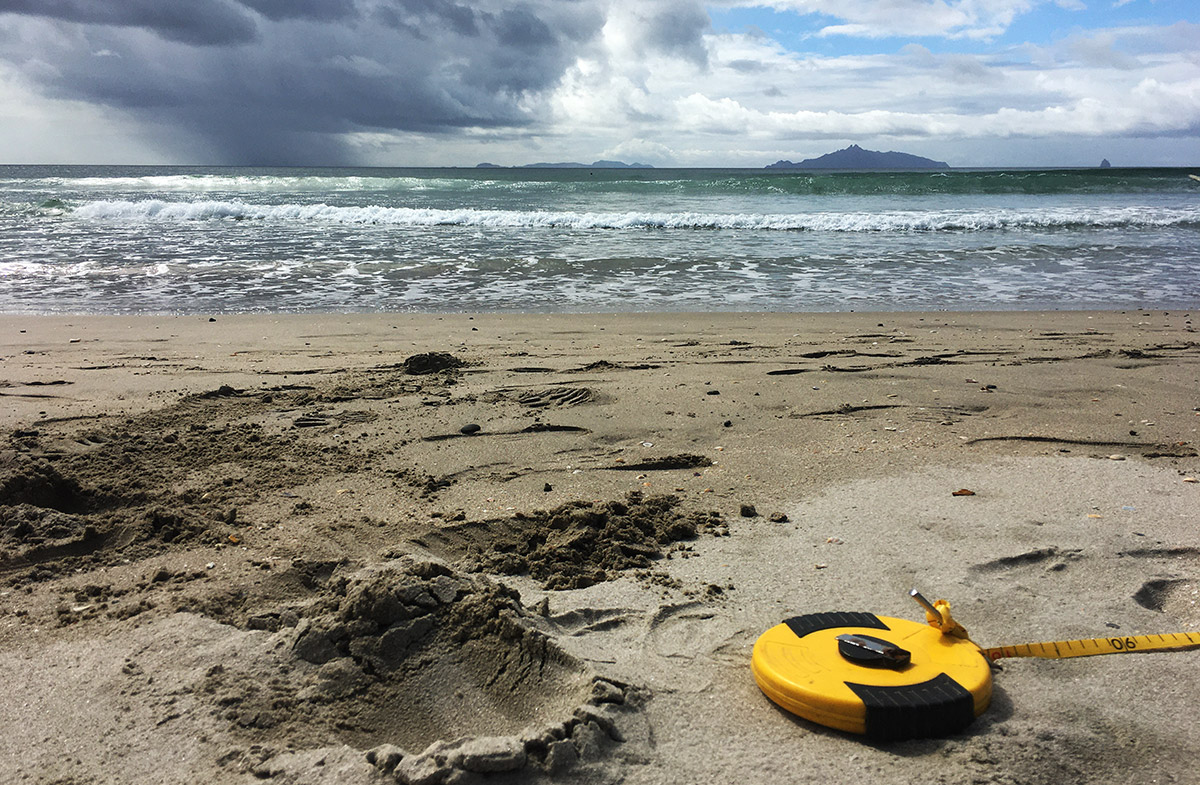 Tape measure on sand with sea in background.