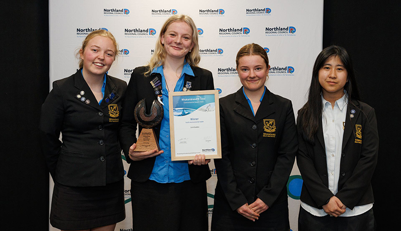 Four female high school students with trophy and certificate in front of Northland Regional Council logo backdrop. (Photo: Dawn Dutton Photography).