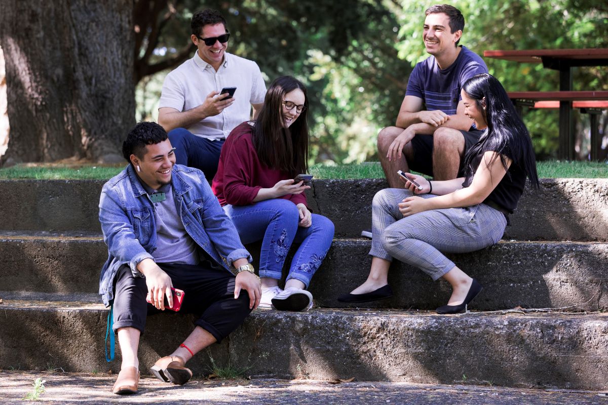 Group of people laughing and sitting on steps in a park.