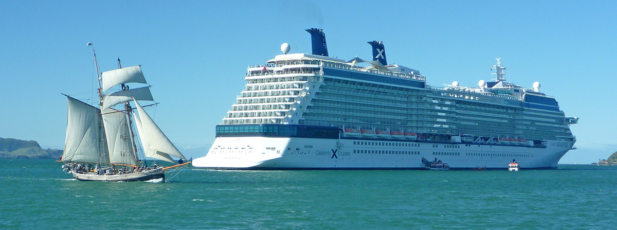 Yacht sailing behind anchored cruise ship.