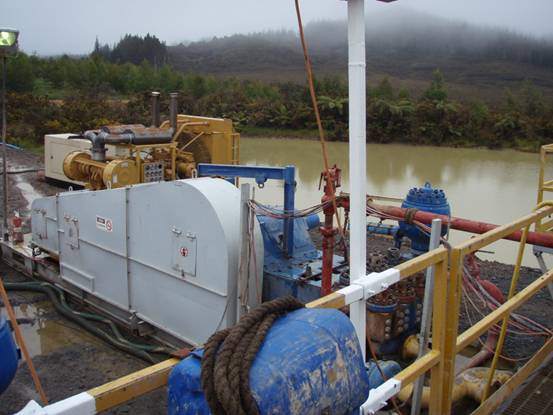 Part of the drilling equipment with discharge pond in background.