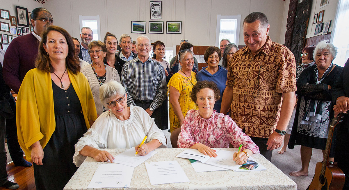 People signing documents while others watch on.