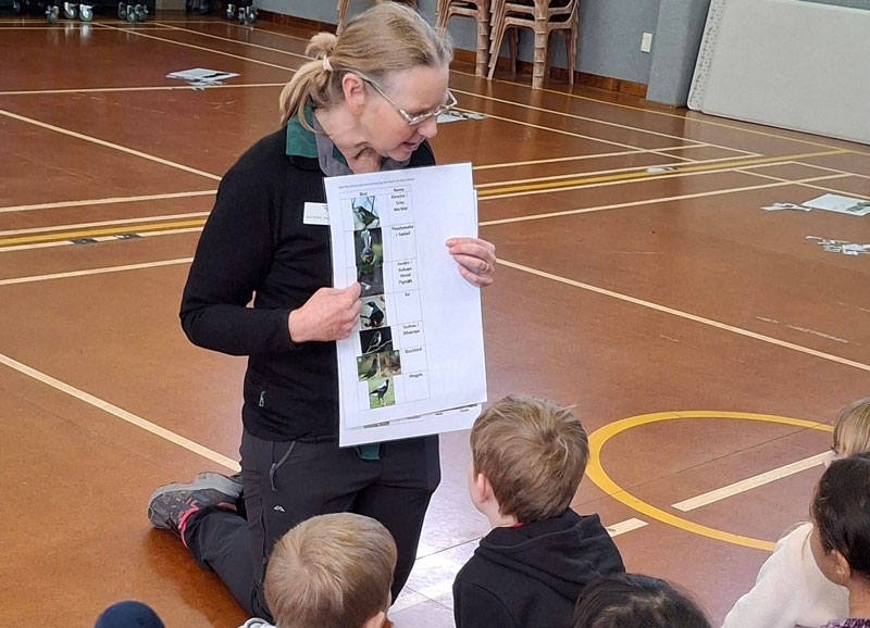 Woman holding piece of paper in front of group of students.