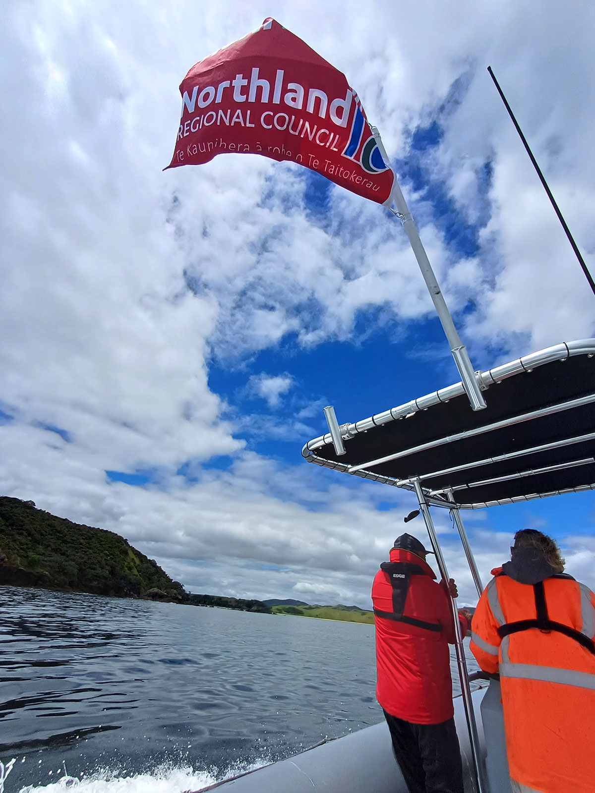 Two men on a boat flying red flag with Northland Regional Council and logo.