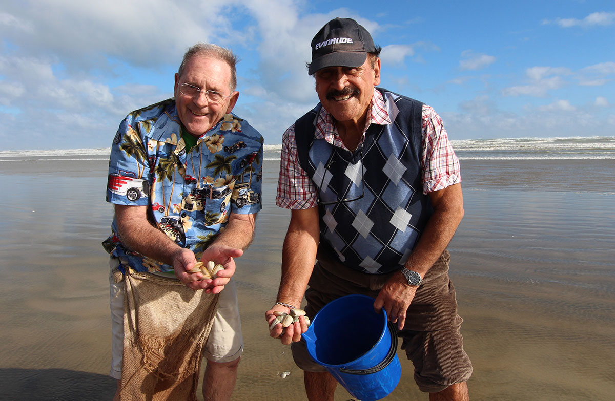 Two men on a beach holding shellfish and a blue bucket.