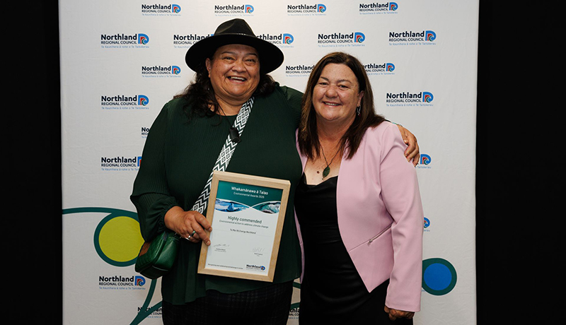 Two women, one wearing a hat and holding a certificate, in front of Northland Regional Council logo backdrop. (Photo: Dawn Dutton Photography).