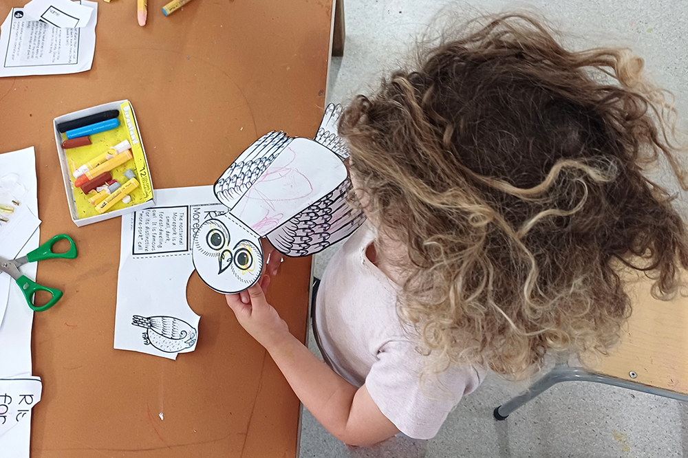 Child making paper owl puppet at a table.