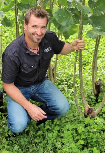 Land Manager Duncan Kervell crouched down holding on to plant smiling.