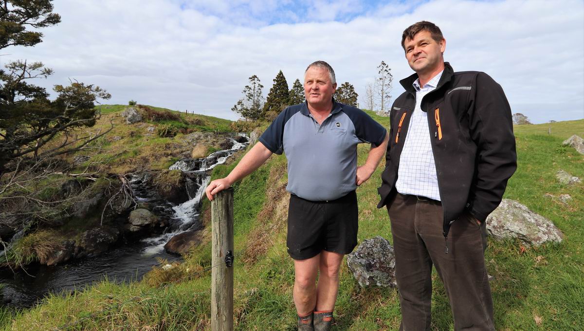 Two men stand by a stream.