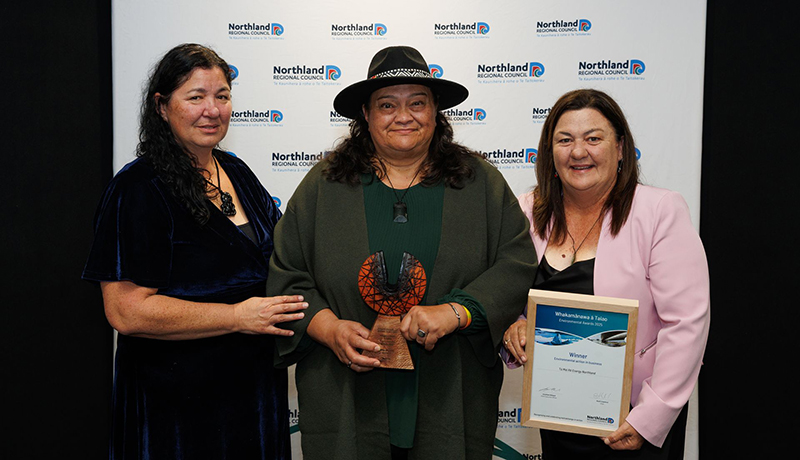 Three women, one wearing a hat, with a trophy and certificate in front of Northland Regional Council logo backdrop. (Photo: Dawn Dutton Photography).