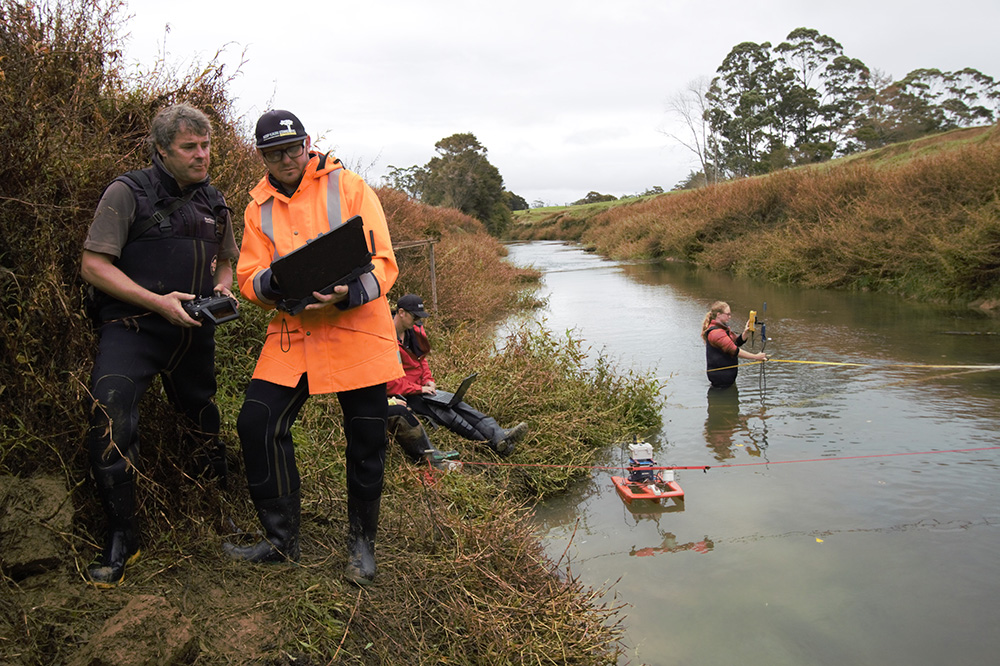 People standing by and in the river using hydrology equipment.