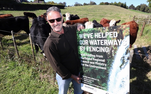 Man holding sign in front of cows in paddock.