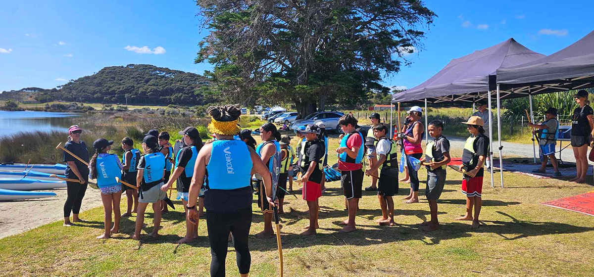 Group of children in lifejackets standing on a grassy bank.