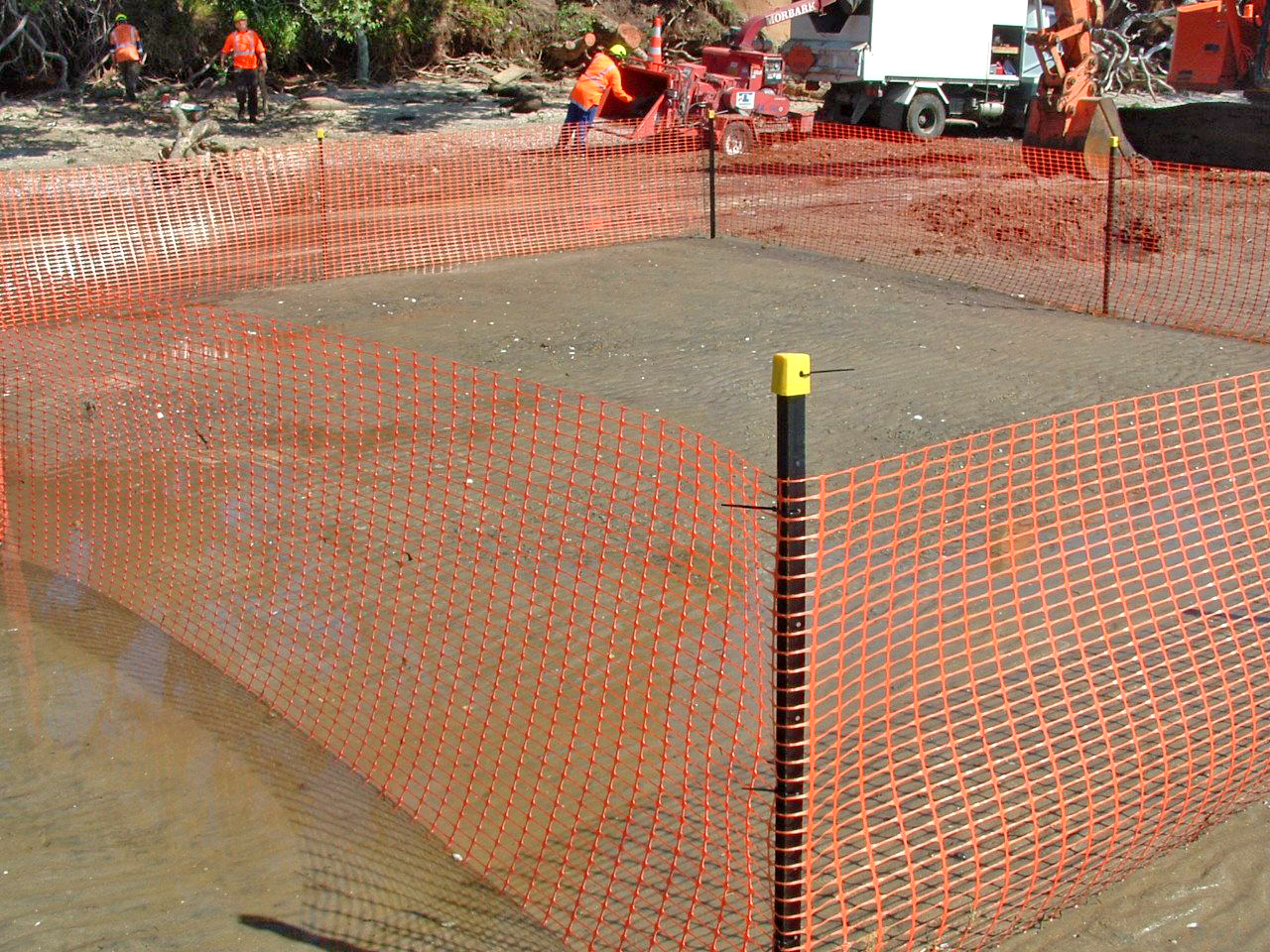 An area of seabed surrounded by orange safety netting with workers in the background.