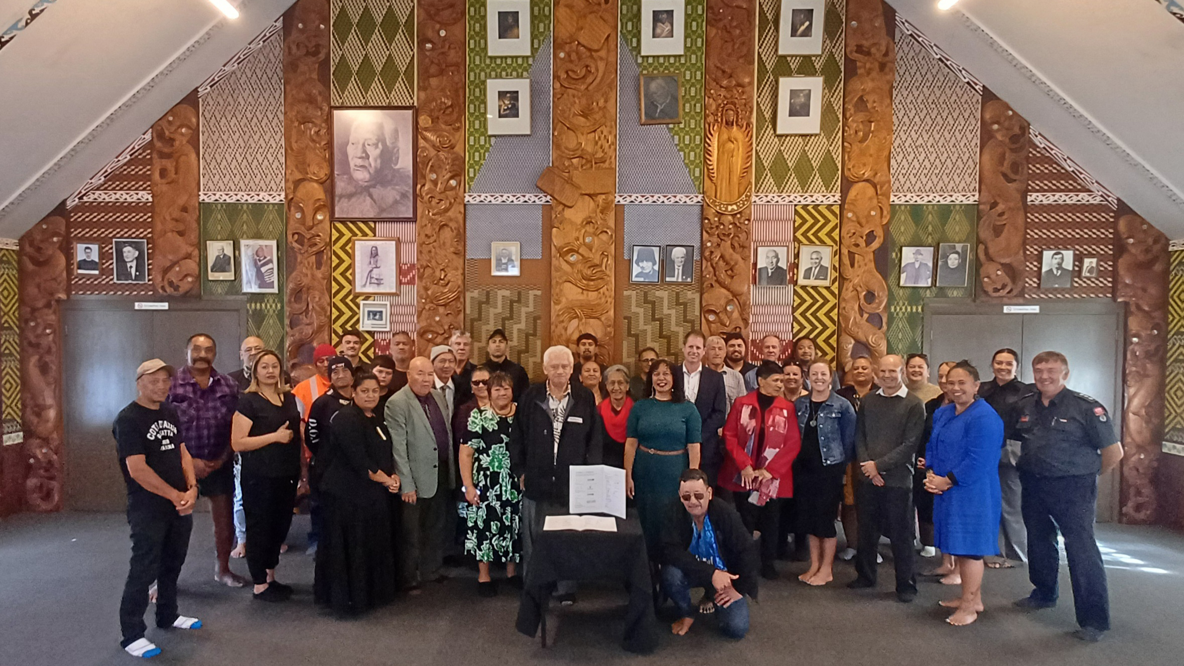 Group of people in the wharenui (meeting house) with the signed agreement in the foreground.