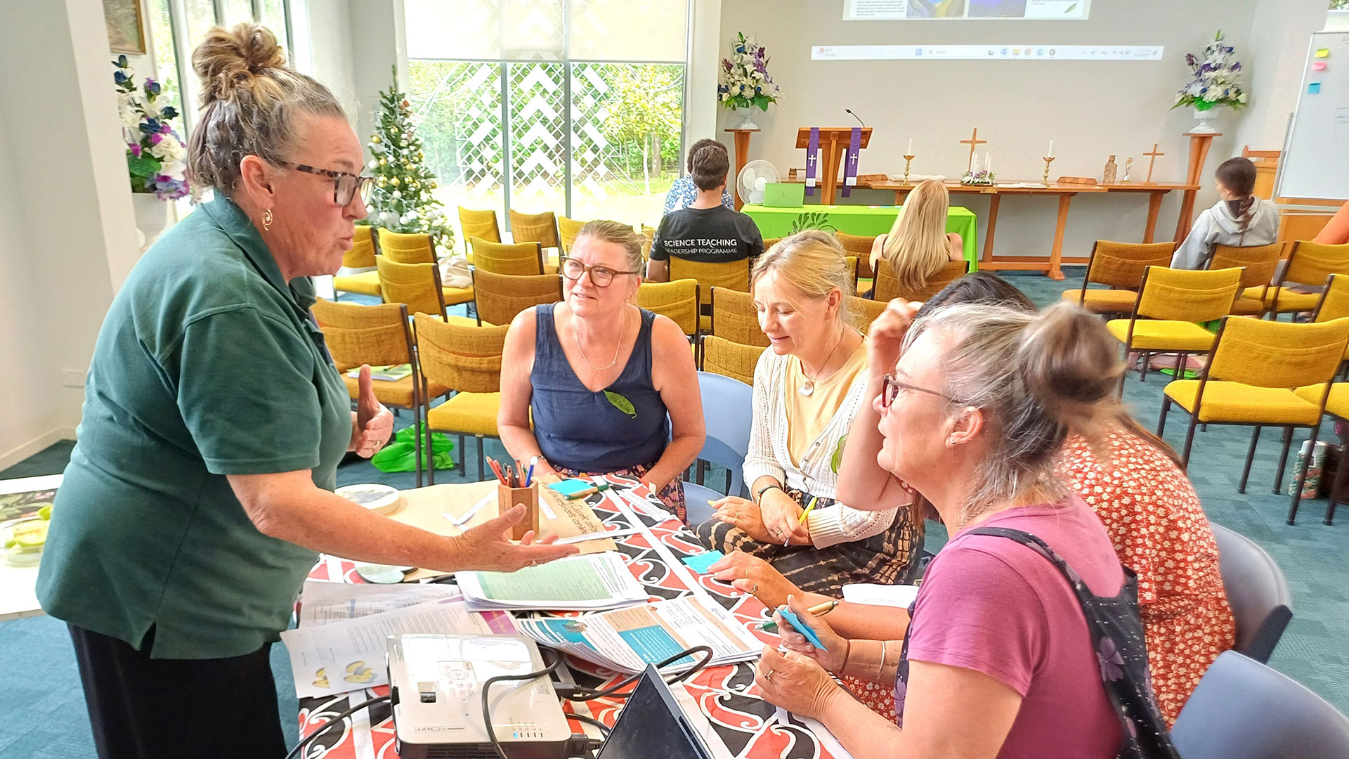 One woman leads a small group discussion during an early childhood climate learning session, using shared resources at a workshop table.