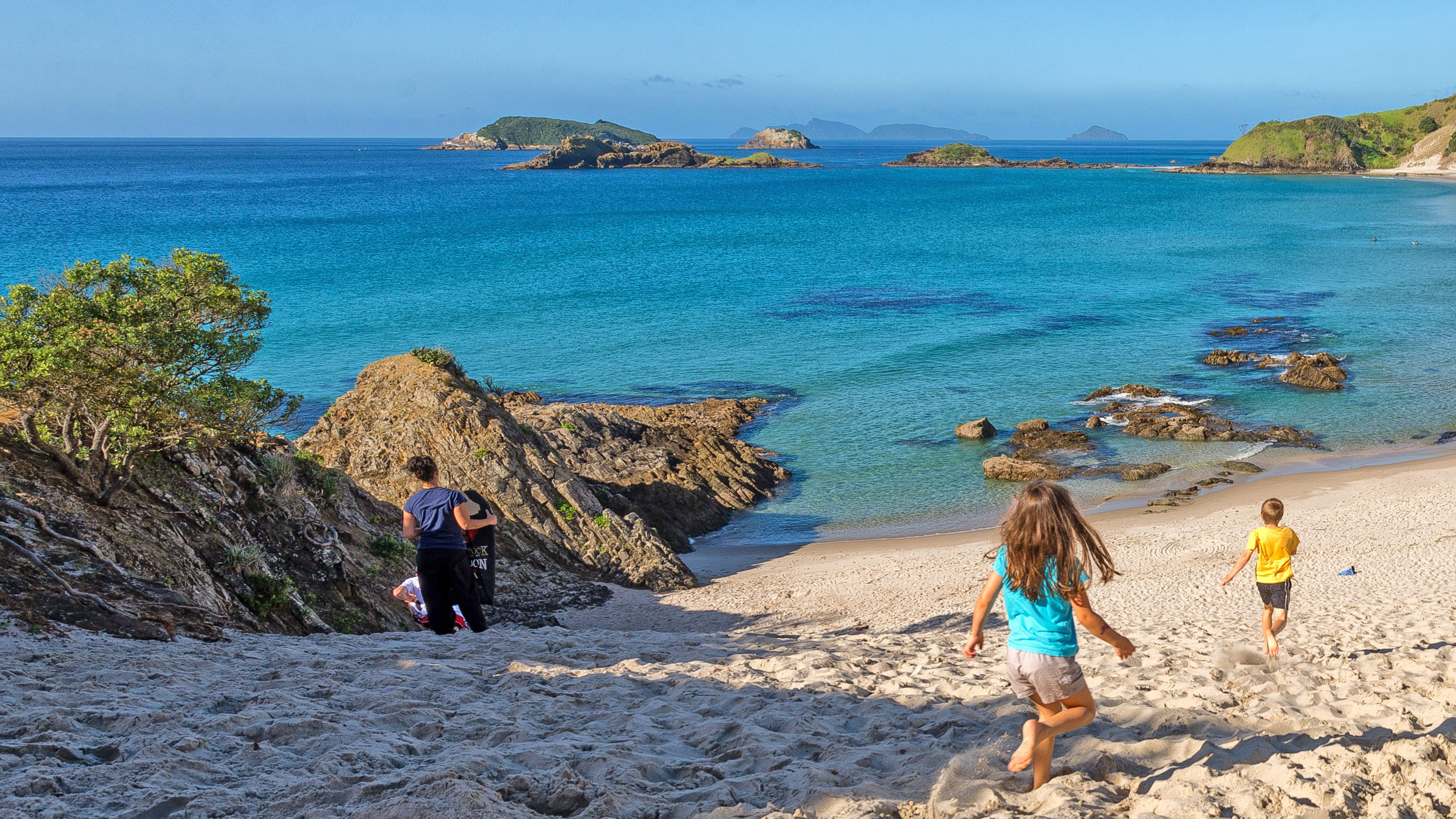 Children running down sand dune toward beach.