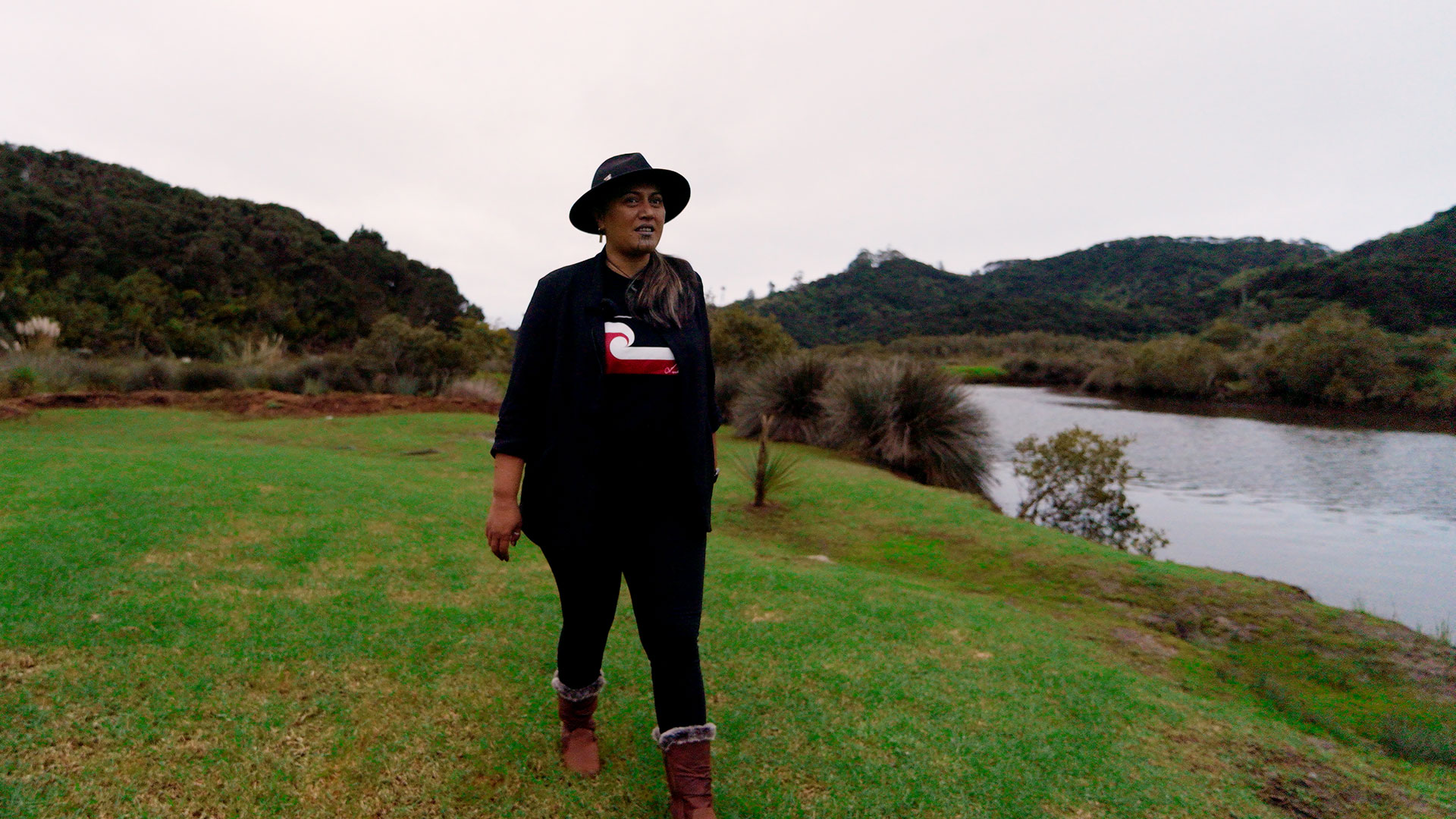 A woman wearing a hat walking alongside a river.