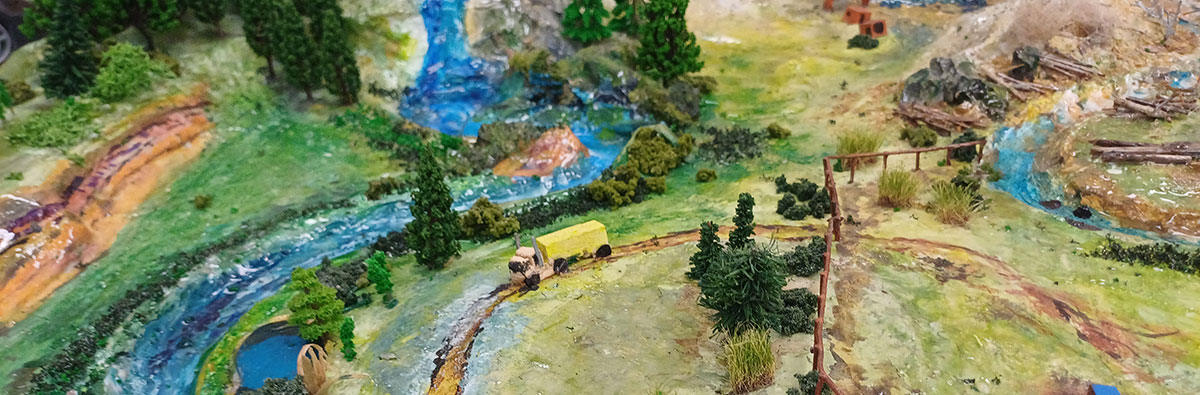 The model of a catchment with a river, bridge, yellow truck, fences and bush.
