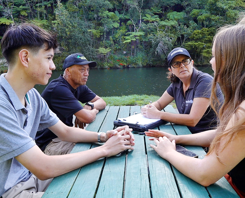 Two men and two women sitting at a picnic table by the river.