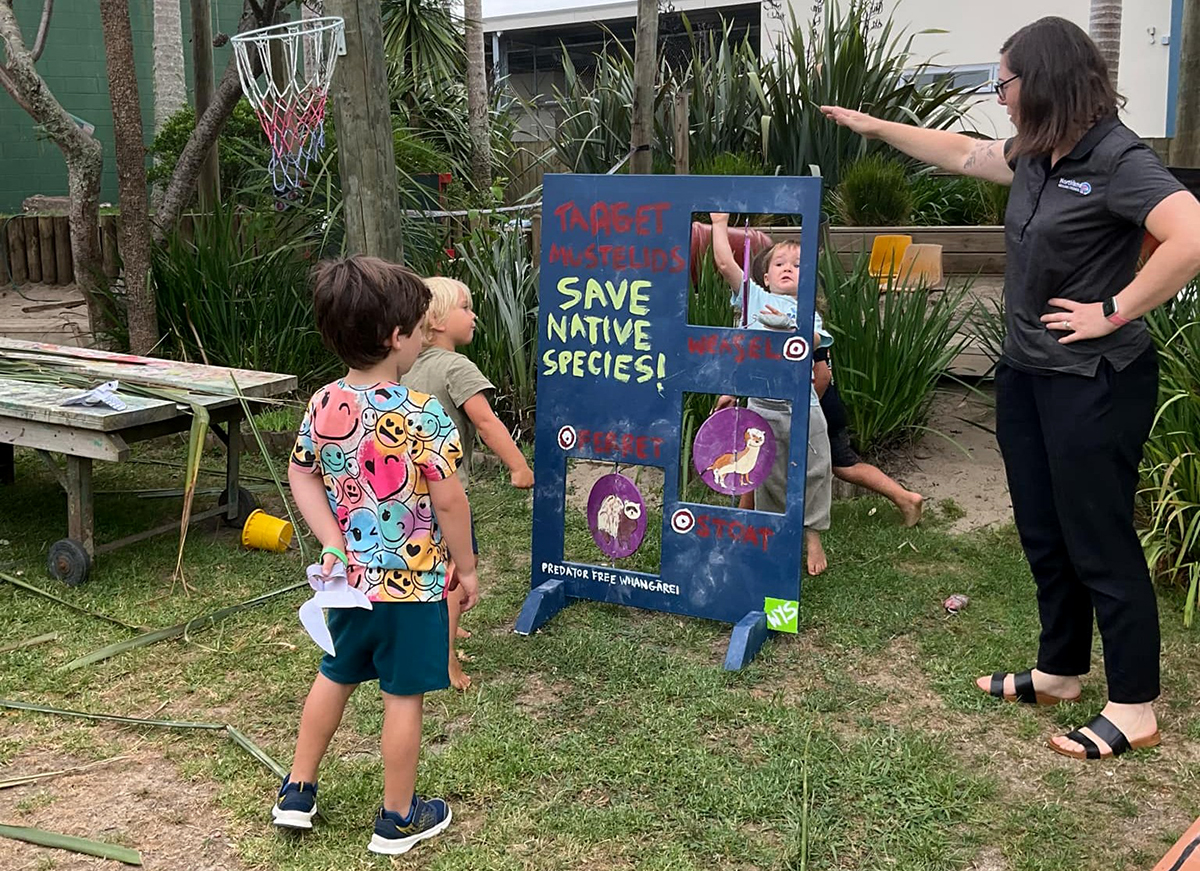 Child and adult stand near a board while throwing bean bags.