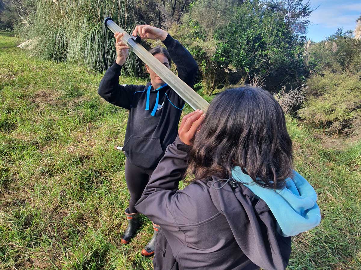 Two students outdoors near a wetland testing a water quality instrument.