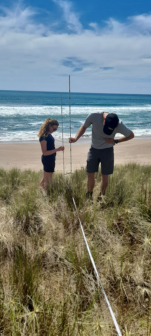 Two people on sand dune with monitoring equipment.