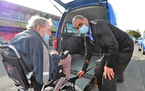 Man in wheelchair being assisted into mobility van.