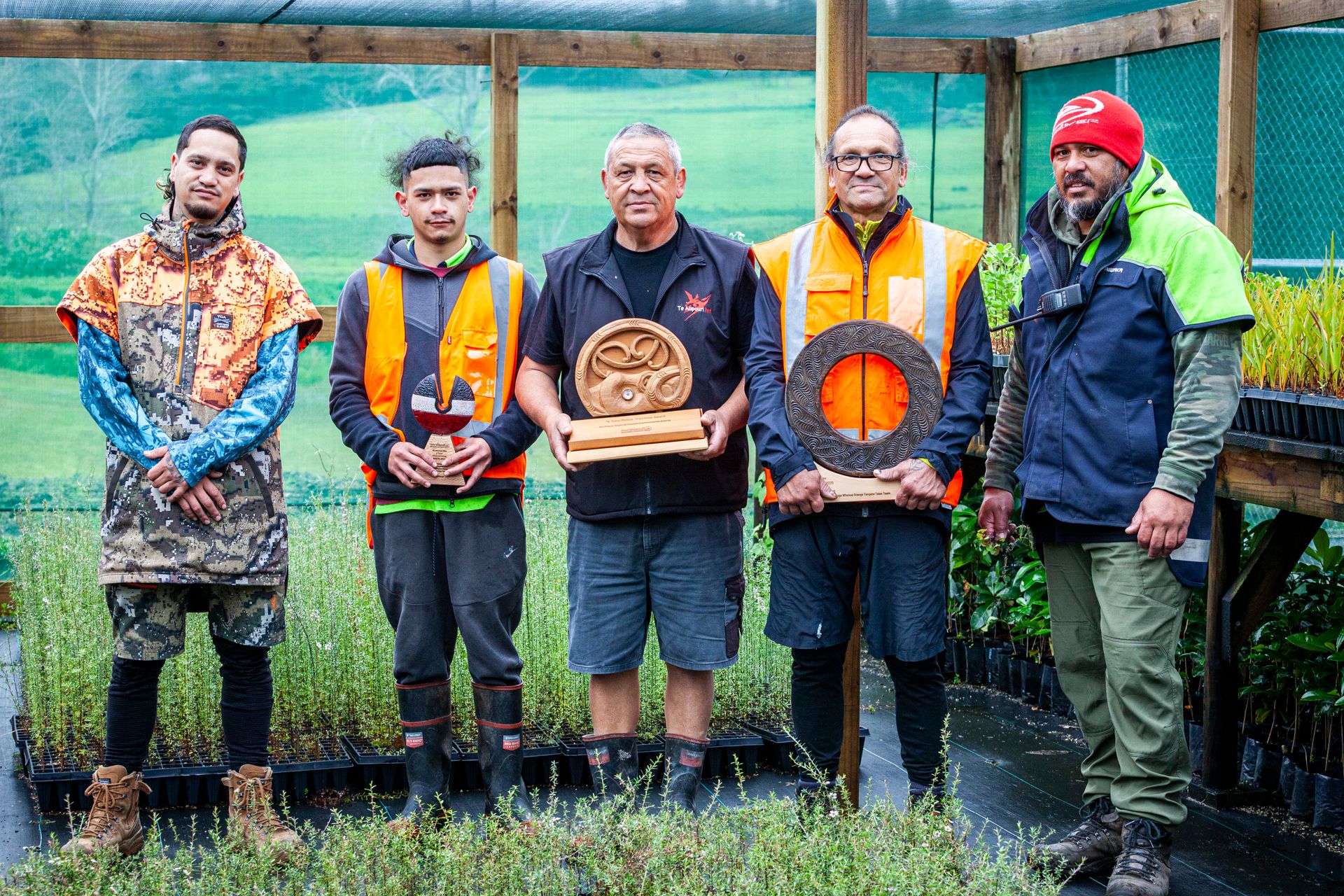 Five men in garden nursery wearing gumboots and hi-vis jackets and holding trophies
