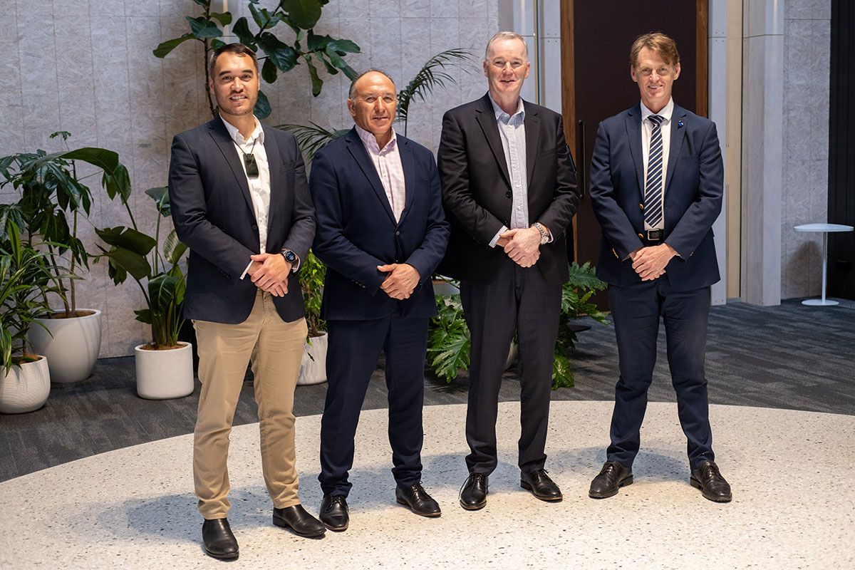 Four men wearing suits in front of a row of pot plants.