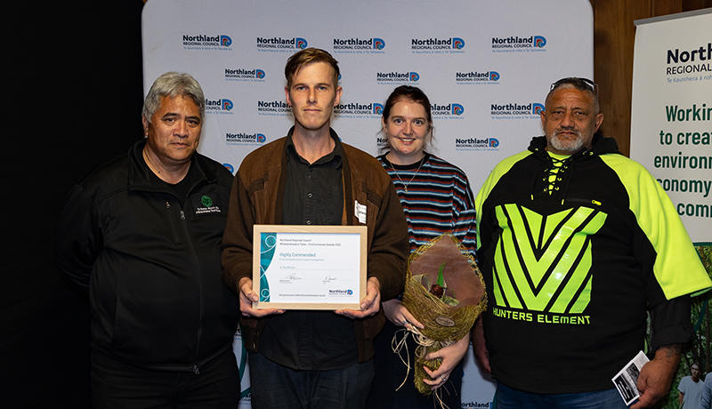 Group of people with certificate and flax flowers.